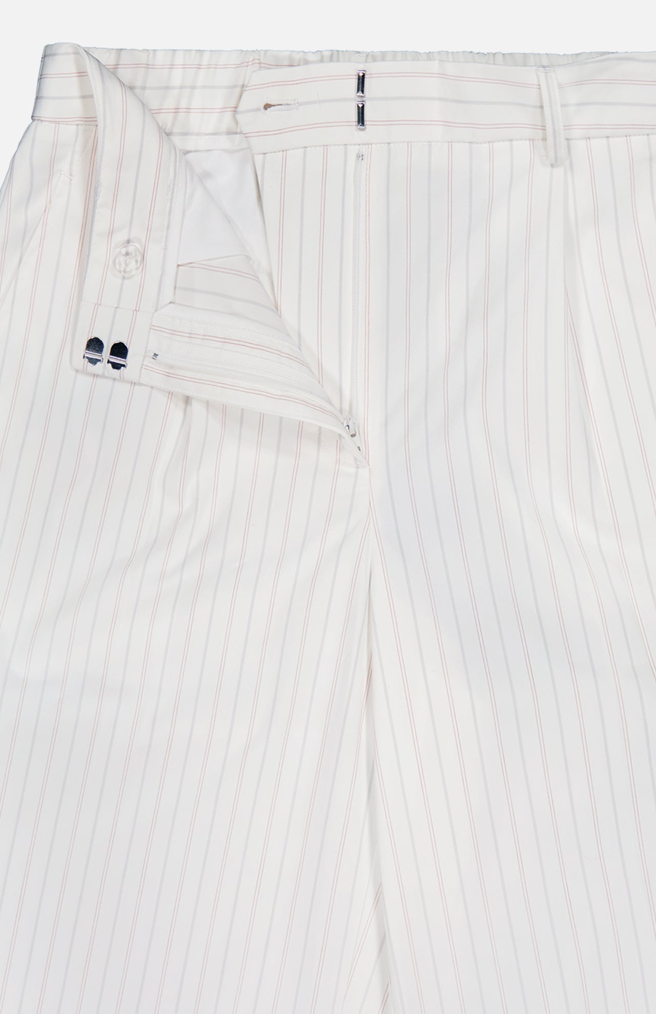 The Hudson St Trouser Pant by TWP features white fabric with thin light red vertical pinstripes. These relaxed pants are styled unbuttoned and partially unzipped, showing the inside waistband and button details.