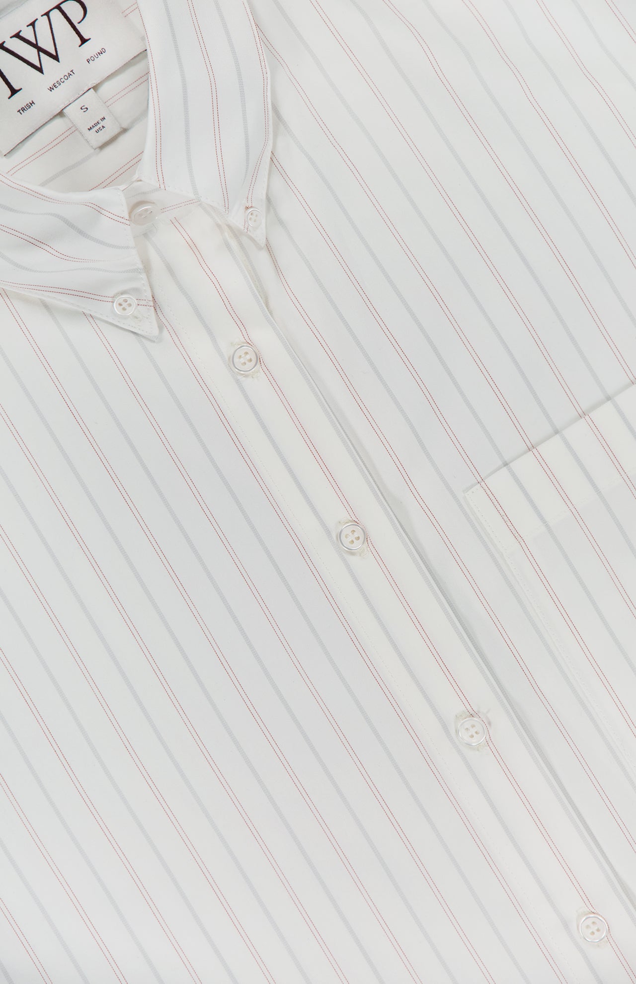 Close-up of the TWP J.D. Shirt—a women's white shirt with thin red vertical stripes, front pocket, and a visible collar label, offering a classic striped workwear style.