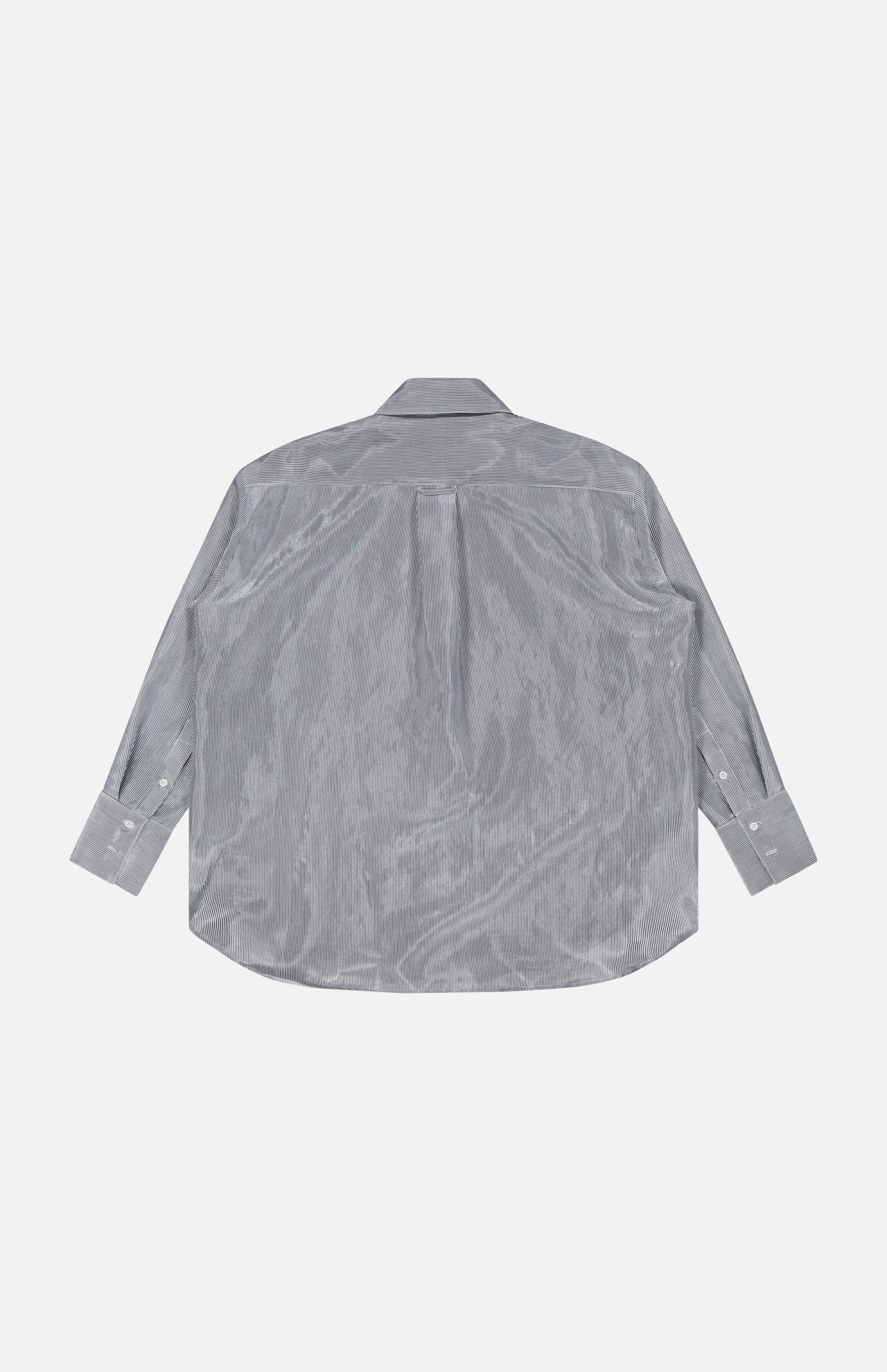 The TWP Big Joe Glossy Stripe Shirt shown flat with the back facing up reveals its yoke and pleat details. This oversized, light gray button-up features long sleeves and is displayed on a plain white background.