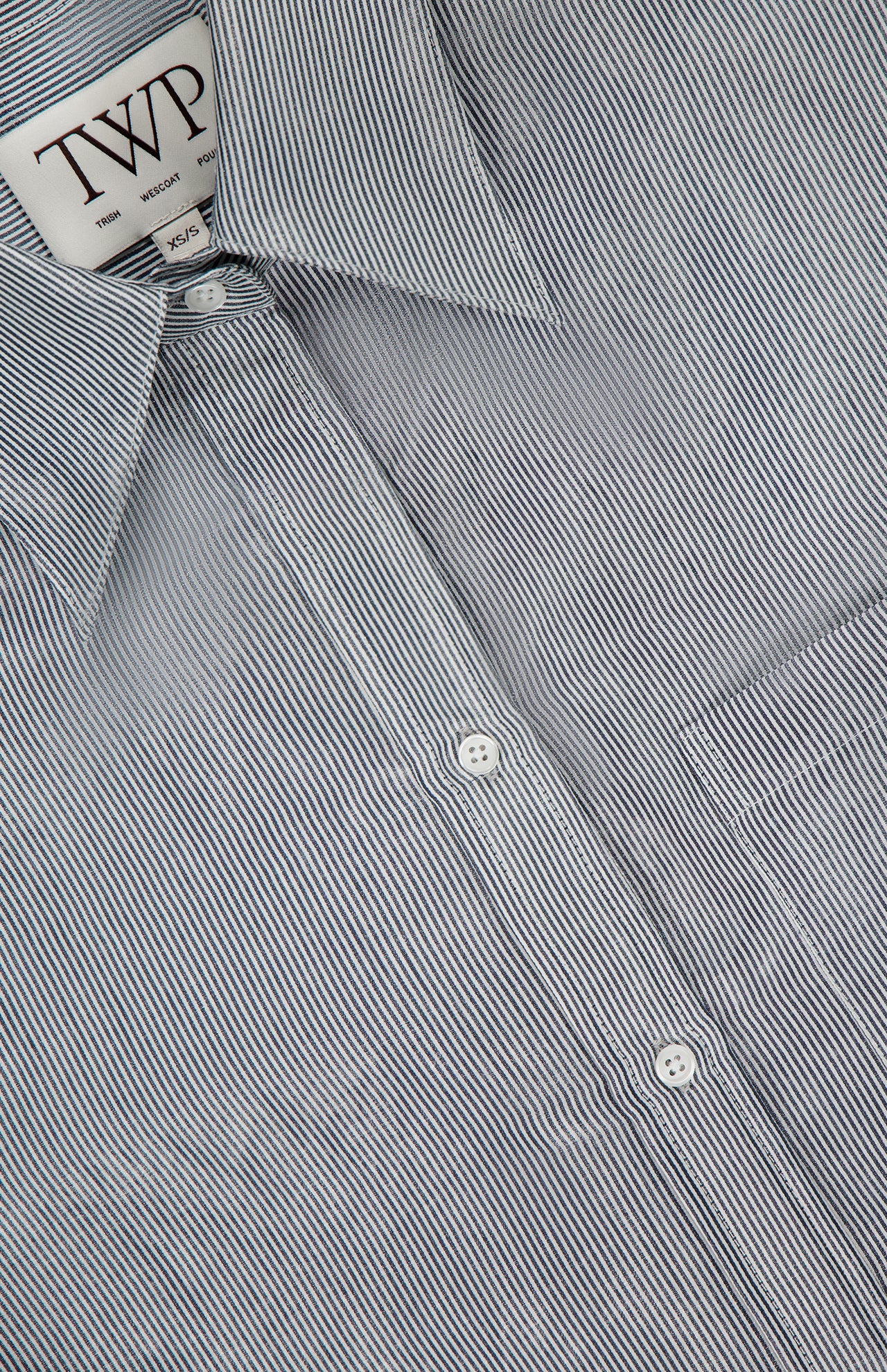 Close-up of the Big Joe Glossy Stripe Shirt by TWP, a black and white pinstriped button-up for women featuring white buttons and a visible TWP XS collar tag—ideal as stylish workwear.