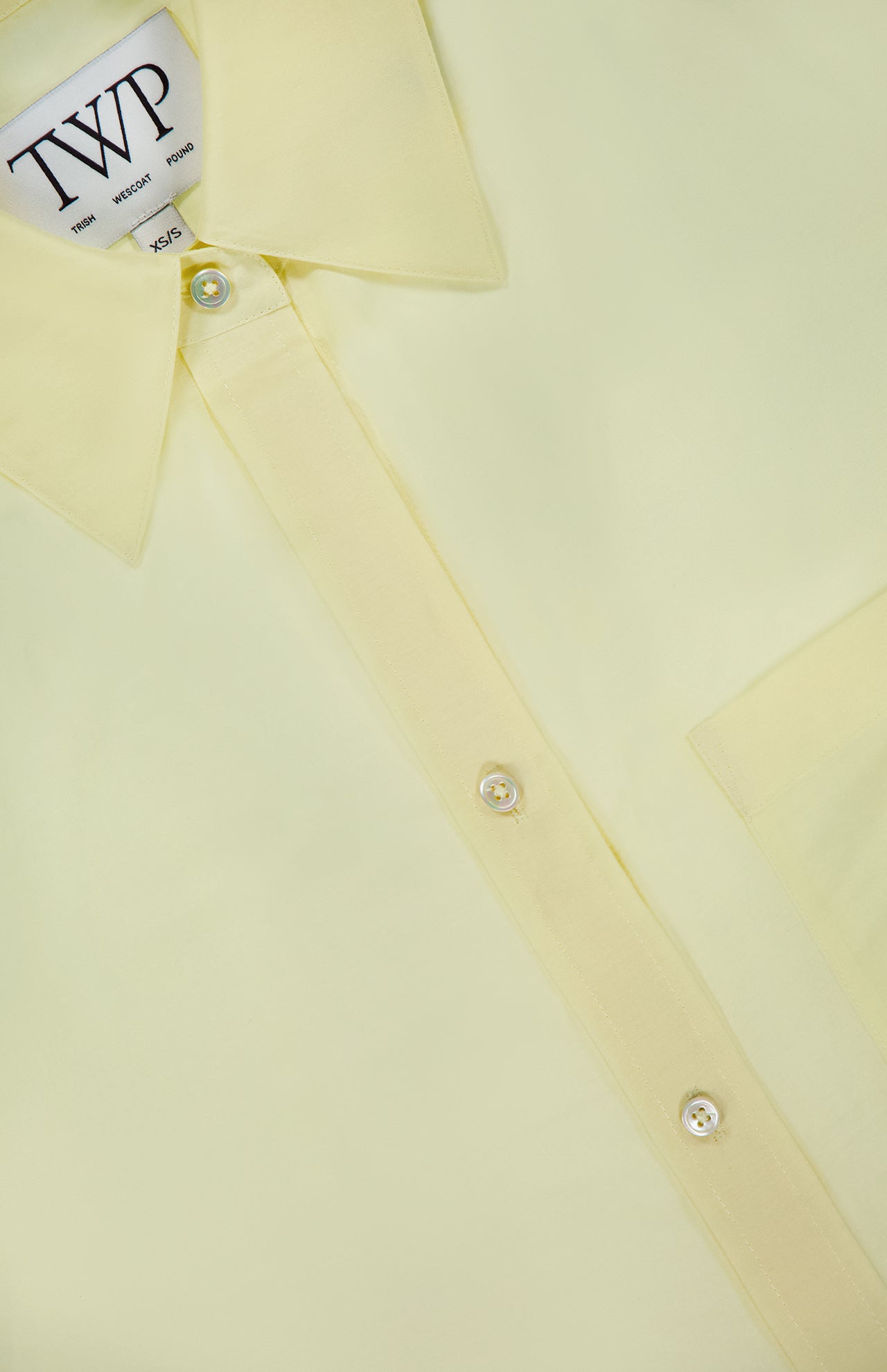 A close-up of the Big Joe Oversized Shirt by TWP, showcasing its pale yellow cotton-silk blend fabric, pointed collar, visible buttons, and chest pocket. The TWP label is visible inside the collar.