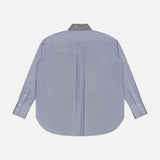 The TWP Big Joe with Crystal Collar Shirt is displayed from the back in light blue, featuring a curved hem and white cuff buttons. The collar stands out with a dark crystal-patterned design, adding a unique detail to this women’s workwear shirt against a plain white background.