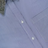 A close-up of the TWP Big Joe with Crystal Collar Shirt, an oversized blue pinstripe design detailed with a silver sequin-embellished crystal collar and a visible chest pocket—an elegant update to modern women’s workwear.