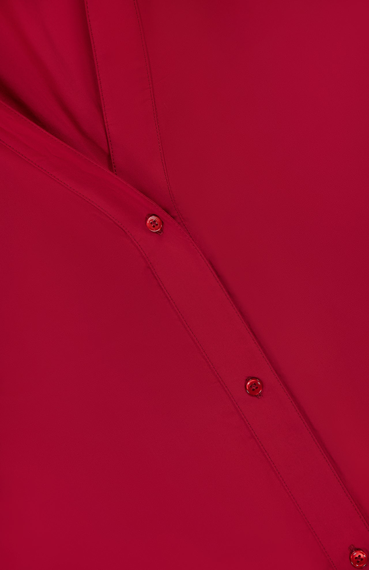 Close-up of TWP's Deep V Relaxed Shirt in red Italian superfine cotton, highlighting two paneled seams and three red buttons. The smooth, neatly stitched fabric suggests refined workwear with a relaxed fit for women.