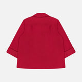 The TWP Deep V Relaxed Shirt, shown from the back in bright red, features a loose fit, long sleeves with folded cuffs, and a straight hem. Made from Italian superfine cotton and set against a plain white background.