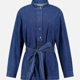 The Denim Tamzin Wrap Shirt by TWP is a long-sleeve blue denim button-up featuring a stand collar and a matching denim waist belt, shown against a plain white background—ideal for versatile women’s workwear or styled as a chic belted wrap jacket.