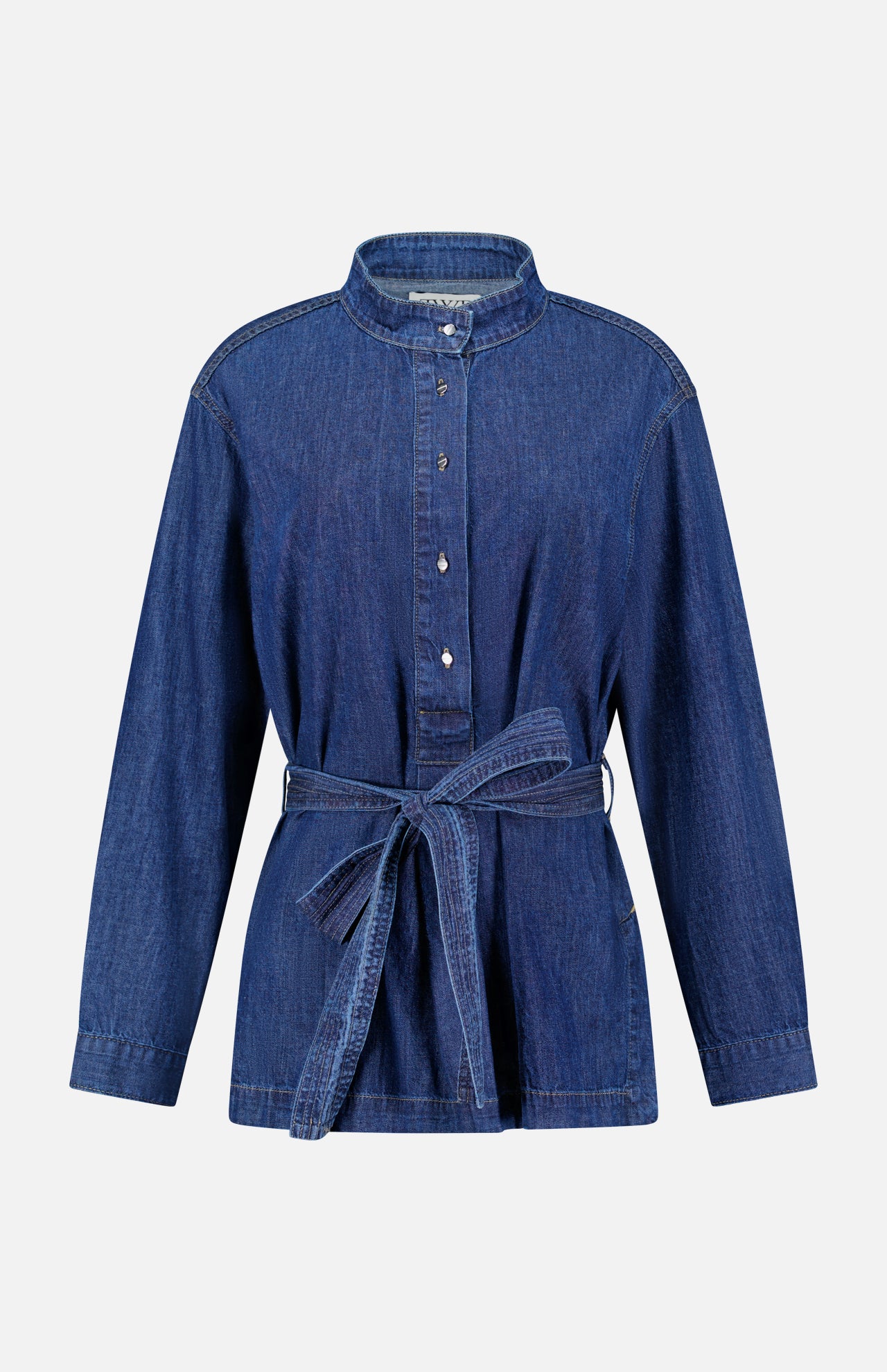 The Denim Tamzin Wrap Shirt by TWP is a long-sleeve blue denim button-up featuring a stand collar and a matching denim waist belt, shown against a plain white background—ideal for versatile women’s workwear or styled as a chic belted wrap jacket.