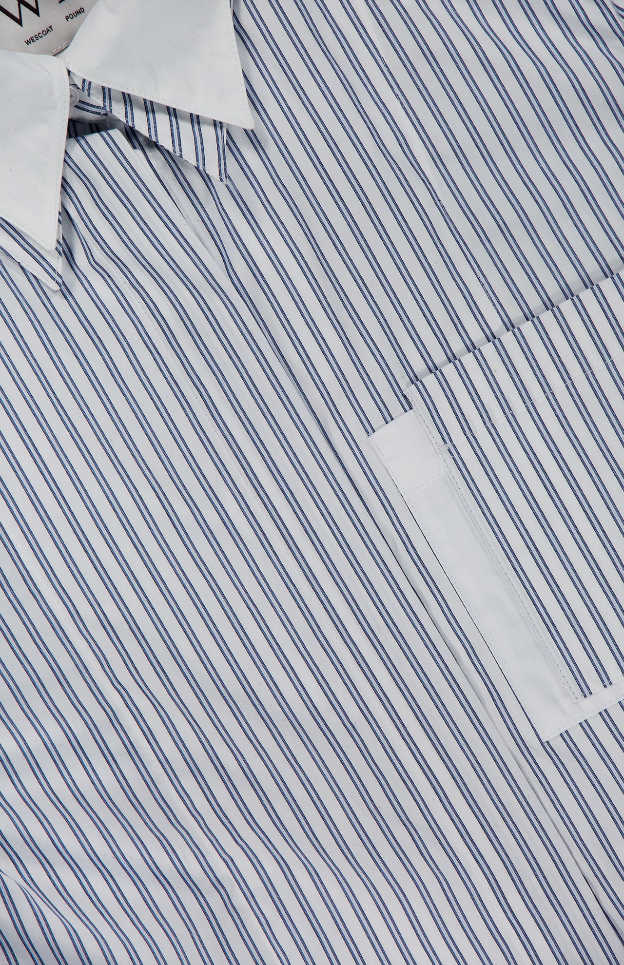 Close-up of the TWP Double Layer Boyfriend Shirt, showcasing a white dress shirt with thin blue vertical stripes, a crisp white collar, and part of a pocket visible.