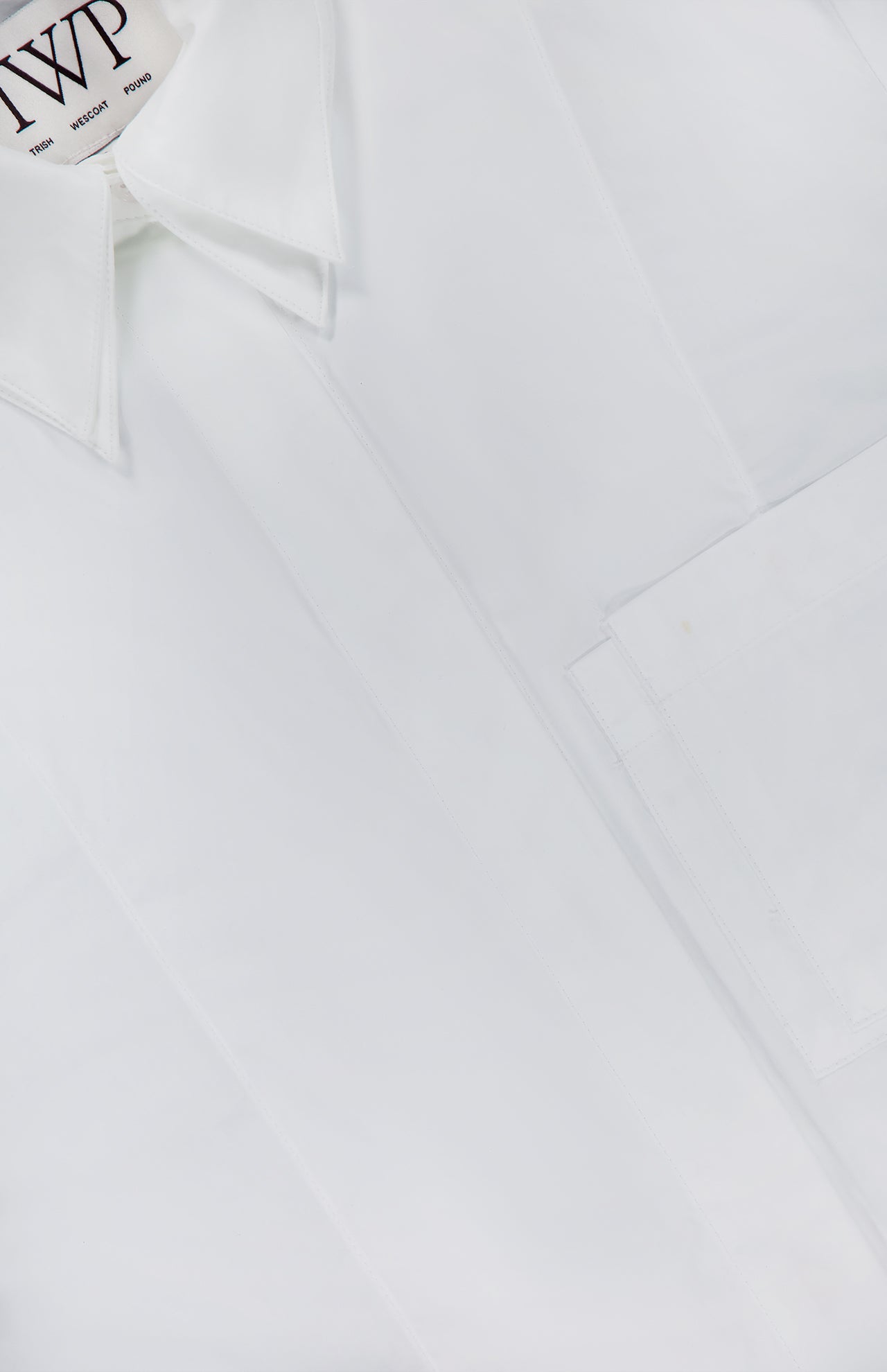 A close-up of the TWP Double Layer Boyfriend Shirt—a crisp white dress shirt for women, showcasing a pointed double collar, front pocket, and a neck label with black text—an essential workwear staple.