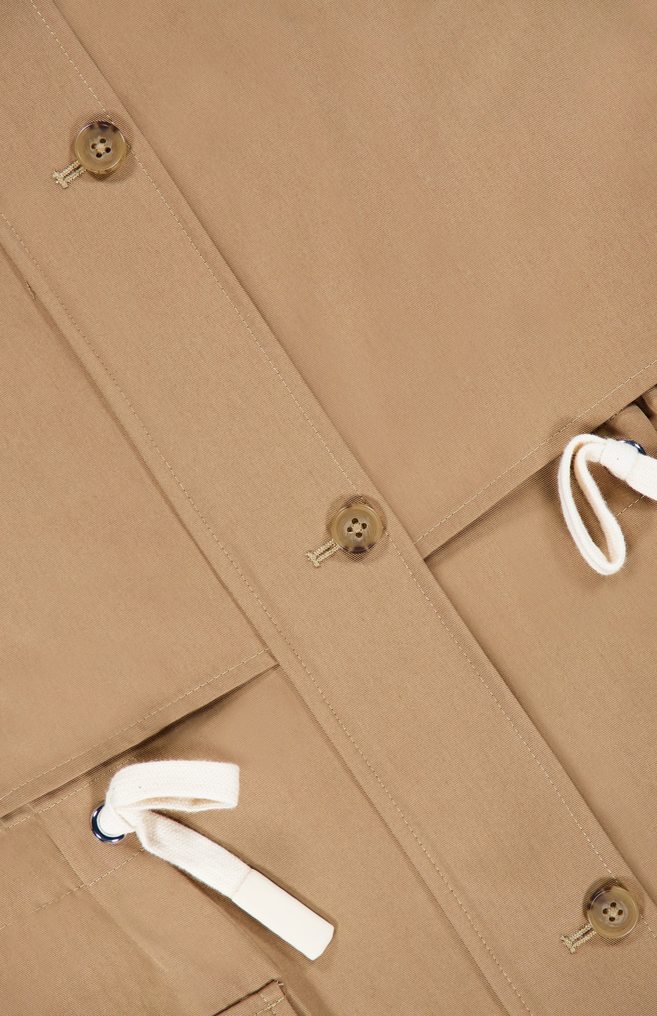 A close-up of the TWP Drawing Conclusions Jacket highlights its beige utility design with brown buttons and white drawstrings, showcasing fabric texture and detailed stitching—a modern take on workwear for women.