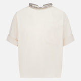The TWP Ex T Shirt With Crystal Collar is a women's short-sleeved, off-white workwear top featuring a single front pocket, turned-up cuffs, and a decorative crystal collar.