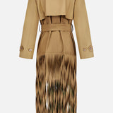 The TWP Fringe Benefit Jacket is a tan trench coat with a belted waist, long fringes at the hem, and buttoned sleeve straps for a stylish, modern look. This water-repellent women’s workwear piece combines fashion and function.