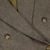 Close-up of the TWP Harper Herringbone Blazer, showcasing its brown herringbone pattern, tortoiseshell buttons, and a hint of olive green lining visible at the collar.
