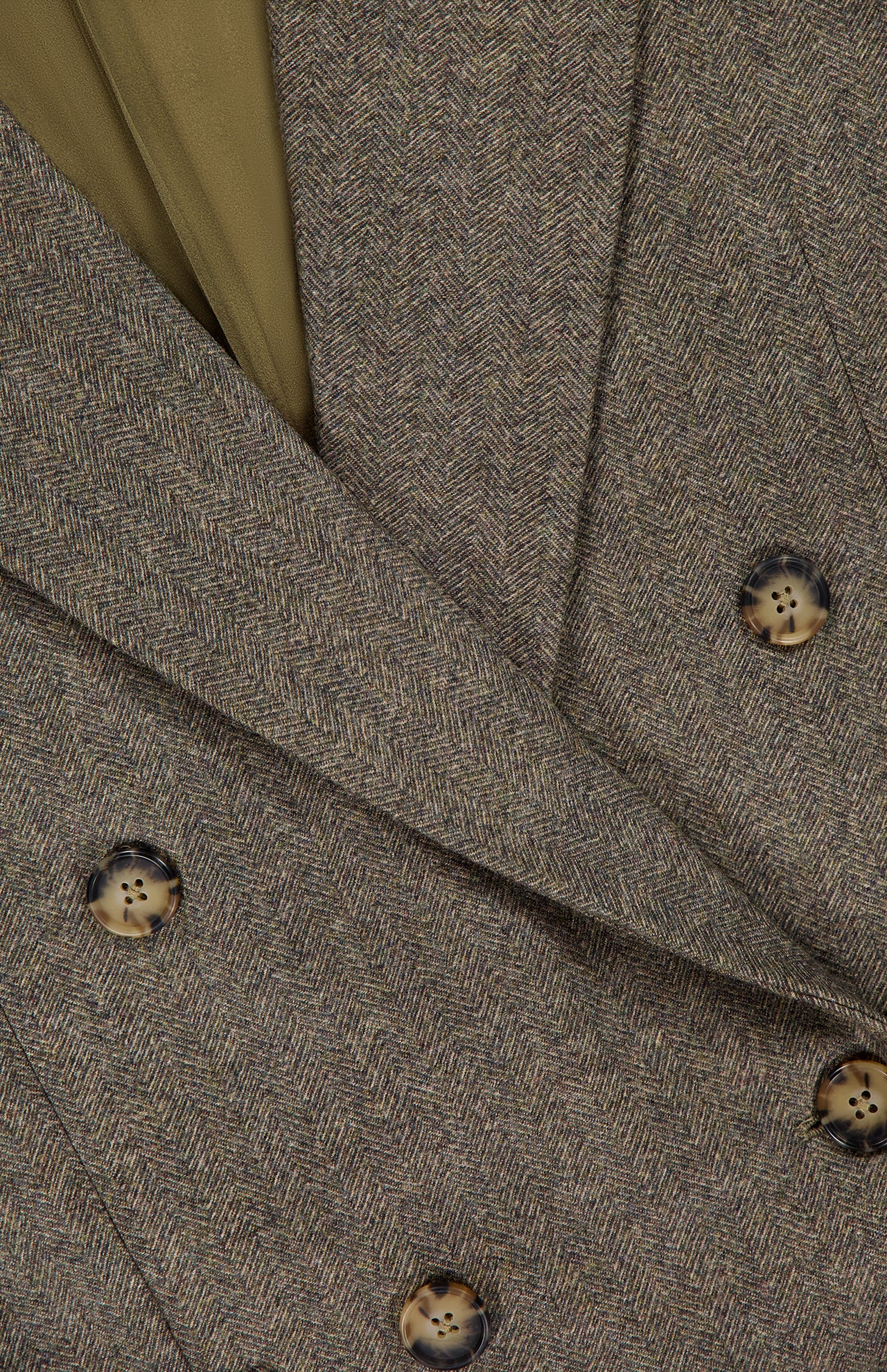 Close-up of the TWP Harper Herringbone Blazer, showcasing its brown herringbone pattern, tortoiseshell buttons, and a hint of olive green lining visible at the collar.
