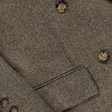 Close-up of the Harper Herringbone Blazer by TWP, highlighting the brown herringbone pattern with three brown buttons on the sleeve and three larger buttons on the front, plus a glimpse of a pocket—an elegant detail characteristic of classic herringbone workwear jackets.