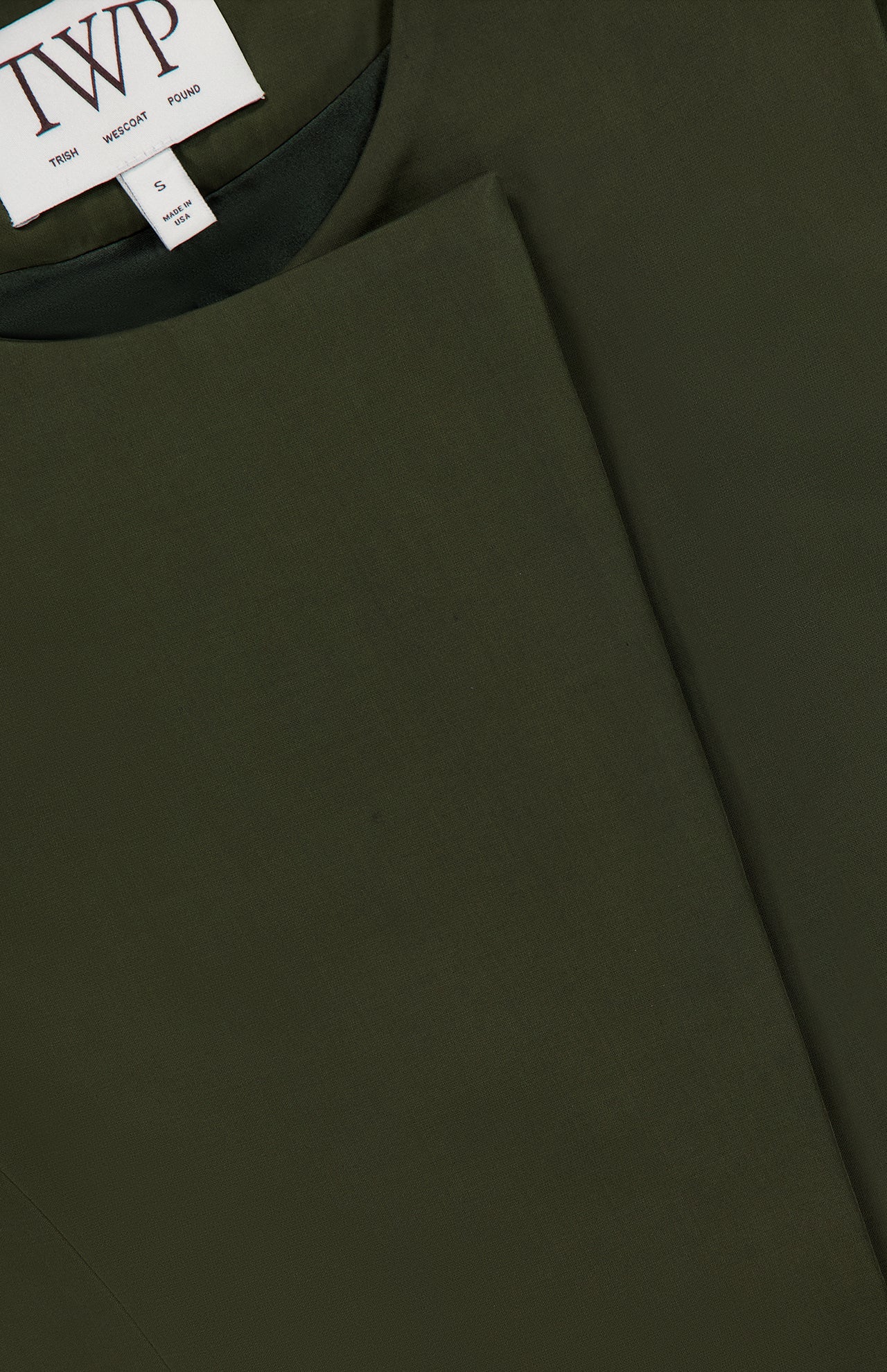 Close-up of a dark green High Neck Hidden Placket Vest with a white clothing label displaying the brand initials TWP and size S. The fabric looks smooth and structured, making it an ideal choice for stylish women's workwear.