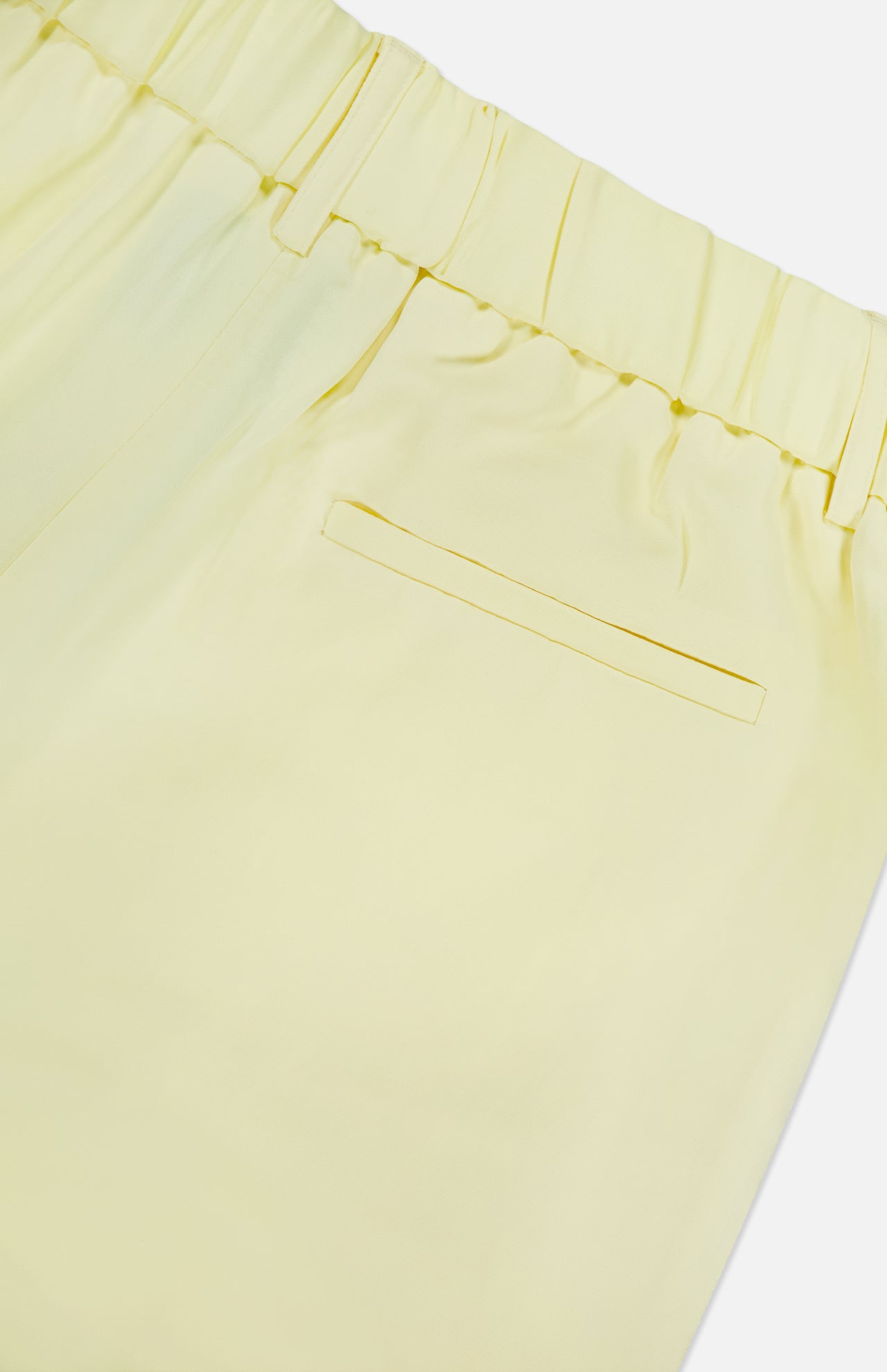 Close-up of the back of TWP’s Hudson St Pleated Pant in light yellow, designed for women with an elastic waistband and a single right welt pocket. The smooth, slightly shiny fabric makes it ideal workwear.