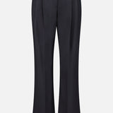 The Ivy Pleated Trouser Pant by TWP showcases a sophisticated workwear option for women, featuring black tailored pants with belt loops, front pleats, and a slight flare at the hem in a mid-rise silhouette, all presented against a plain white background.