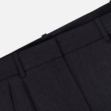 Close-up of the waistband and upper section of the TWP Ivy Pleated Trouser Pant, crafted from dark Italian wool, featuring belt loops, pleats, and part of the pocket against a white background. These mid-rise pants offer sophisticated workwear style for women.