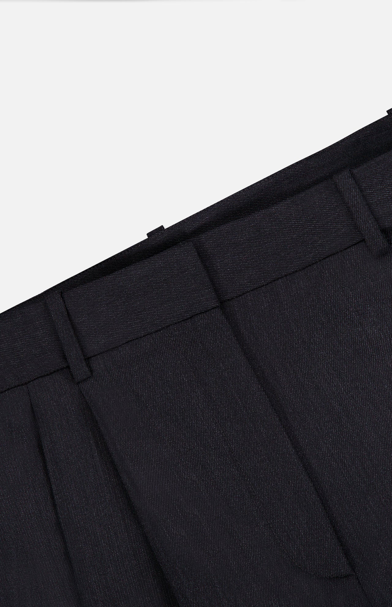 Close-up of the waistband and upper section of the TWP Ivy Pleated Trouser Pant, crafted from dark Italian wool, featuring belt loops, pleats, and part of the pocket against a white background. These mid-rise pants offer sophisticated workwear style for women.