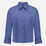 The TWP J.D.S Cropped Shirt is a women's boxy fit, long sleeve blue shirt with a collar, chest pocket, and wide cuffs, shown against a plain white background.