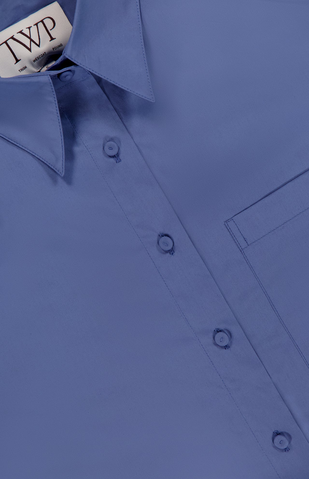 A close-up of the J.D.S Cropped Shirt by TWP, featuring a visible collar, buttons, part of a chest pocket, and an inner collar label displaying the brand name TWP.
