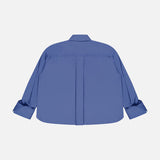 The TWP J.D.S Cropped Shirt is a blue women’s work shirt with a boxy fit, box pleat, and buttoned cuffs, shown from the back and laid flat on a white background.