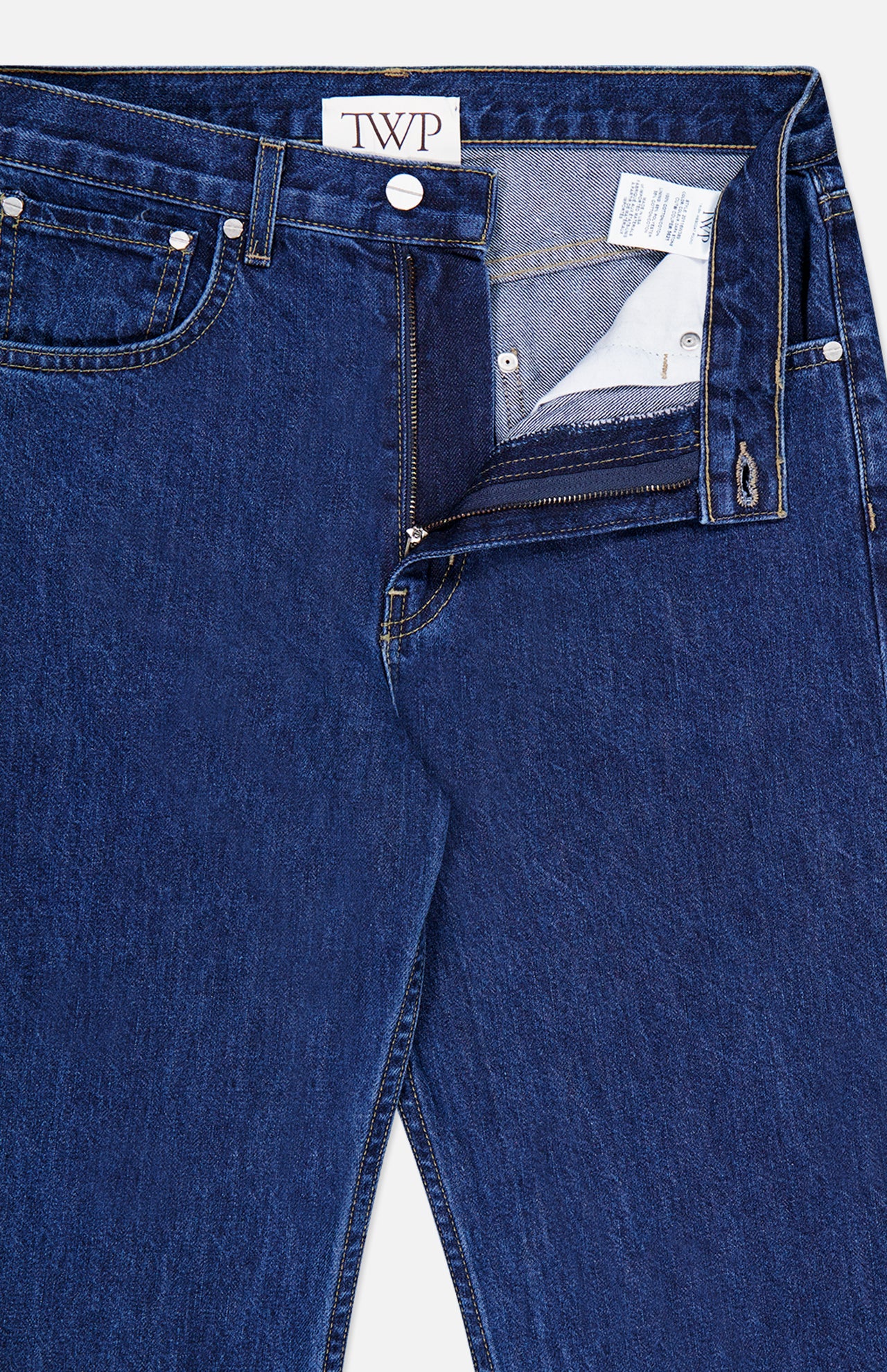 A pair of TWP Kent St Jean in Dark Stone women’s denim jeans is pictured with the zipper and button open, revealing the inside waistband and pocket label. These jeans showcase classic stitching, a straight leg silhouette, and a TWP brand tag on the inner waistband.