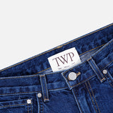 Close-up of the Kent St Jean in Dark Stone by TWP, showcasing a white label with bold TWP lettering on the inside of the waistband. The classic straight leg style features visible front pockets, belt loops, and metal rivet accents.