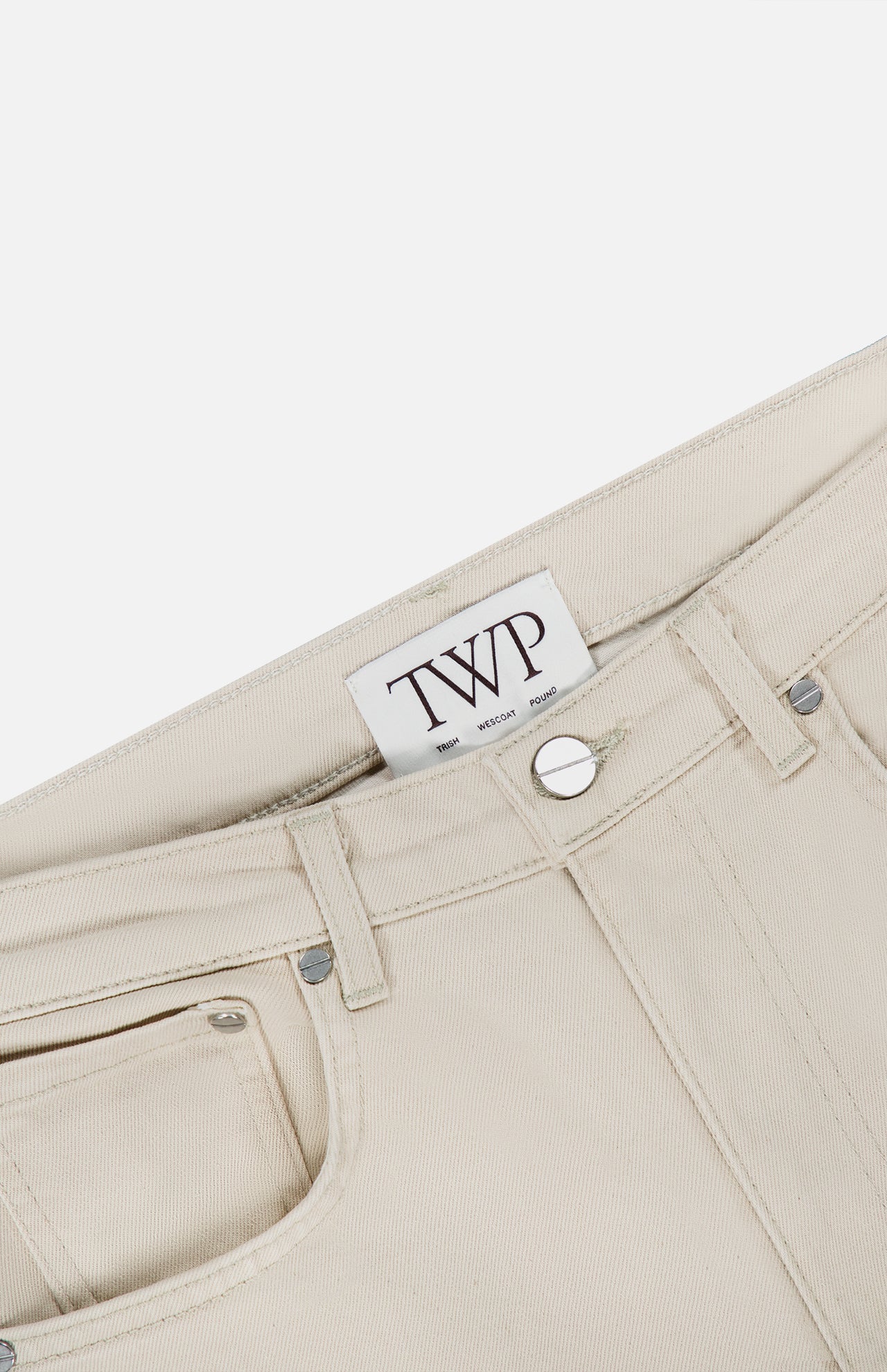 Close-up of the Kent St Pant in Bone, featuring a visible TWP brand label, silver button, belt loops, and pocket against a white background; these women’s straight leg pants offer a classic mid-rise fit.