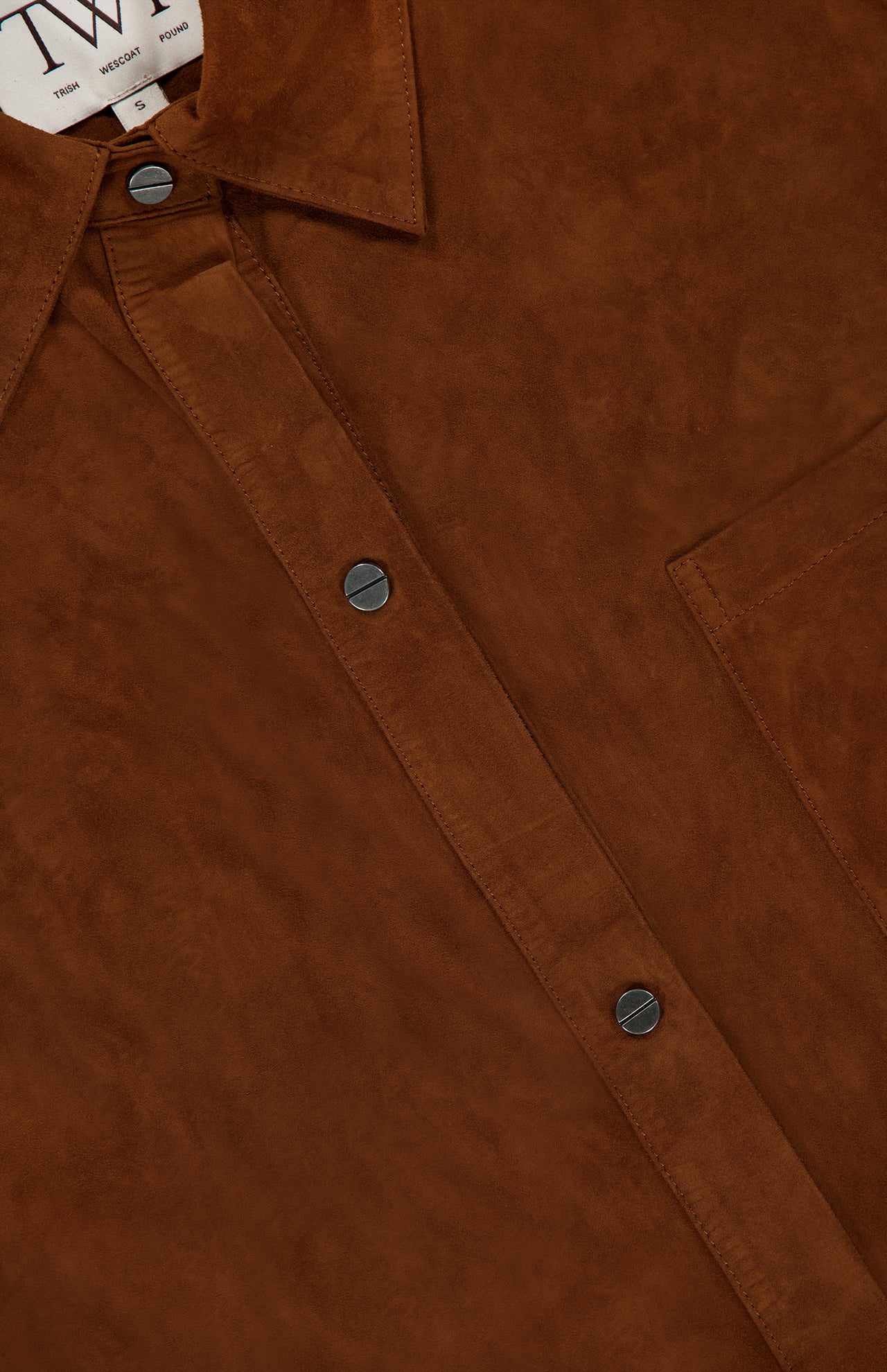 Close-up of the TWP Little Big Joe Jacket—a brown suede shirt jacket for women featuring black snap buttons, a chest pocket, and a partially visible collar label—an elevated reinterpretation of classic workwear.