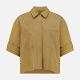 The My Newest Mistake Top by TWP is a short-sleeved Italian cotton blouse in light brown, featuring a collar, relaxed fit, two front chest pockets, and folded sleeve cuffs. Shown against a plain white background.