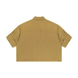 The TWP My Newest Mistake Top is a khaki short-sleeve button-up shirt in Italian cotton, with a relaxed, boxy fit, straight hem, and buttoned sleeves—women’s workwear shown from the back on a plain white background.