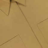 Close-up of the My Newest Mistake Top by TWP—a tan, relaxed fit button-up with two front pockets and a pointed collar. Features a white label with the TWP brand; perfect as a versatile workwear staple for women.