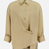 The TWP New Earl Asymmetric Button Front Shirt is a beige Italian cotton long-sleeve with chest pocket and buttoned cuffs, shown on a plain white background—an ideal women’s workwear piece.