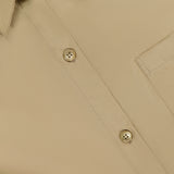 Close-up of the TWP New Earl Asymmetric Button Front Shirt in beige Italian cotton, featuring two buttons, part of a collar, a chest pocket, and a partially visible clothing tag in the upper left corner.