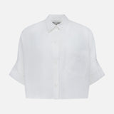 The TWP Next Ex Shirt in Linen is a white, cropped, boxy women's shirt with short sleeves, a collar, front pocket, and cuffs—perfect for workwear and shown against a plain background.