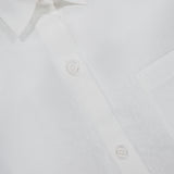 Close-up of the Next Ex Shirt in Linen by TWP—a crisp white, cropped boxy shirt featuring a collar, three white buttons, front pocket, and a modern twist on classic women’s workwear style.
