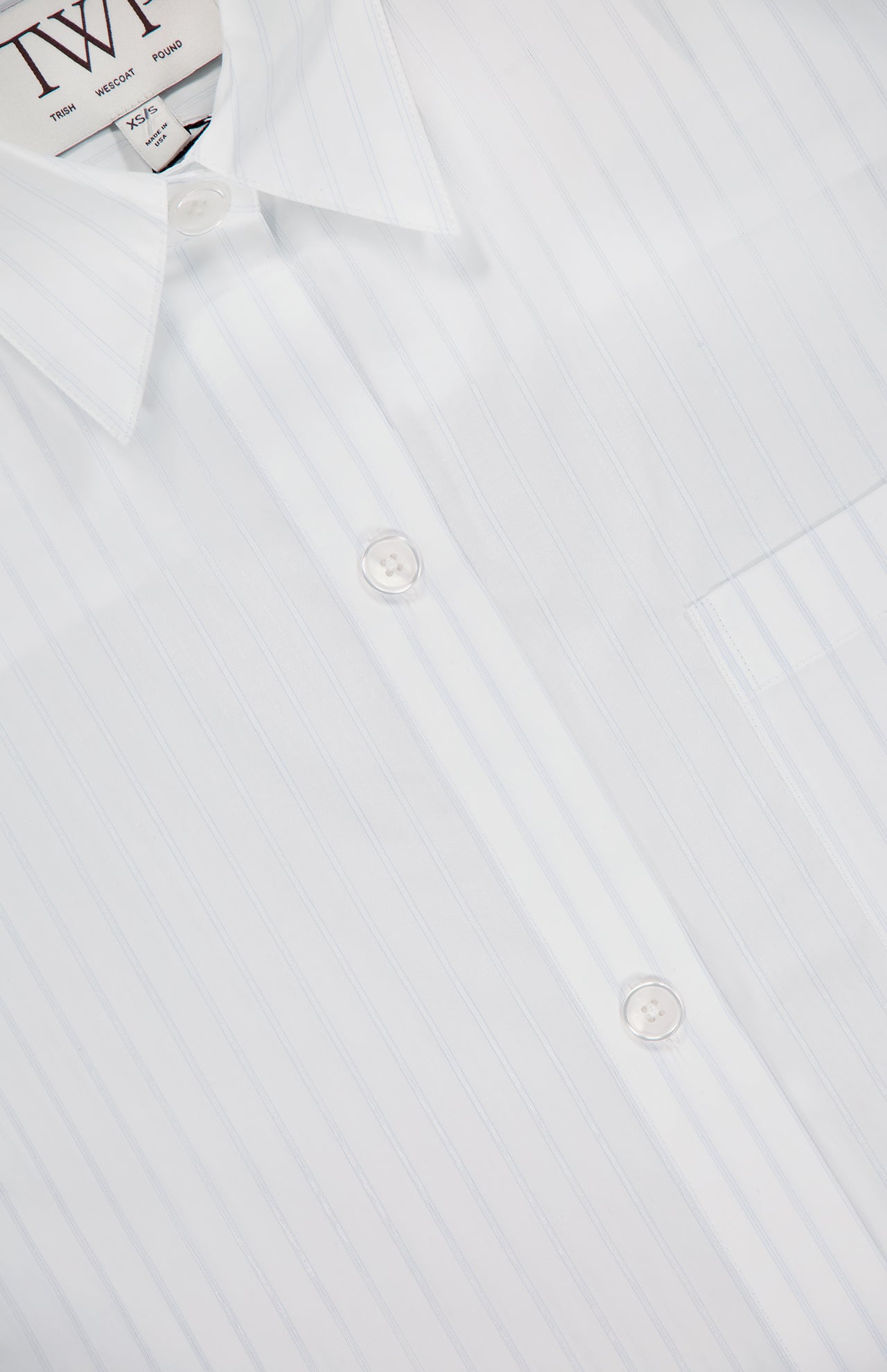Close-up of the TWP Next Ex Cropped Stripe Shirt, featuring subtle vertical pinstripes, white buttons, and a right-side pocket—an elegant women's workwear choice. The collar and clothing label are visible at the top left.