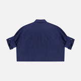 The TWP Next Ex Ruffle Blouse is a navy blue, short-sleeve collared cropped shirt with a relaxed fit and button-tab rolled sleeves—ideal workwear for women who value comfort and style. Shown from the back.