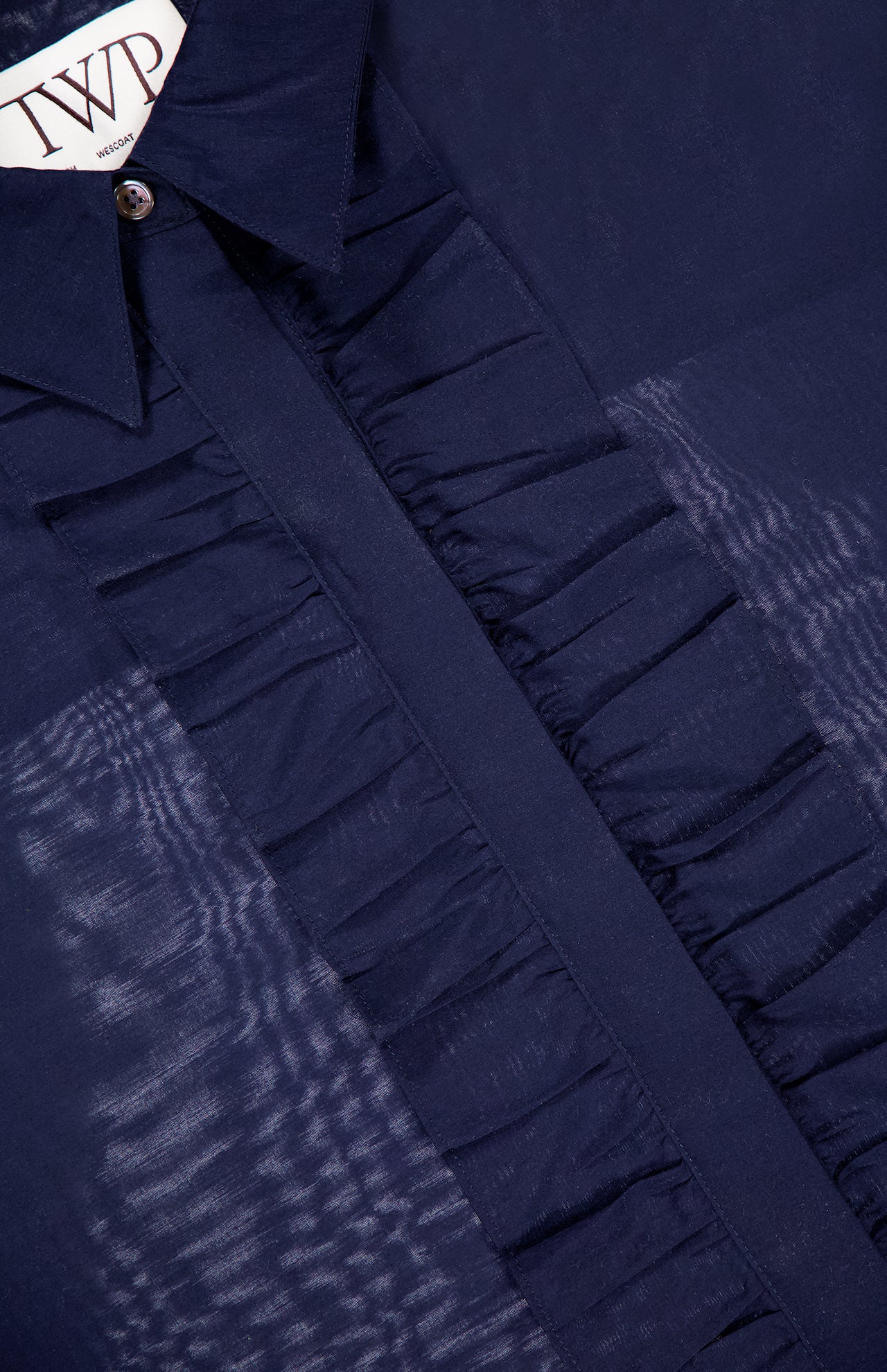 Close-up of the TWP Next Ex Ruffle Blouse in dark blue with a sheer finish, ruffled placket, and pointed collar. The TWP label is visible at the neckline—a stylish workwear choice for women.