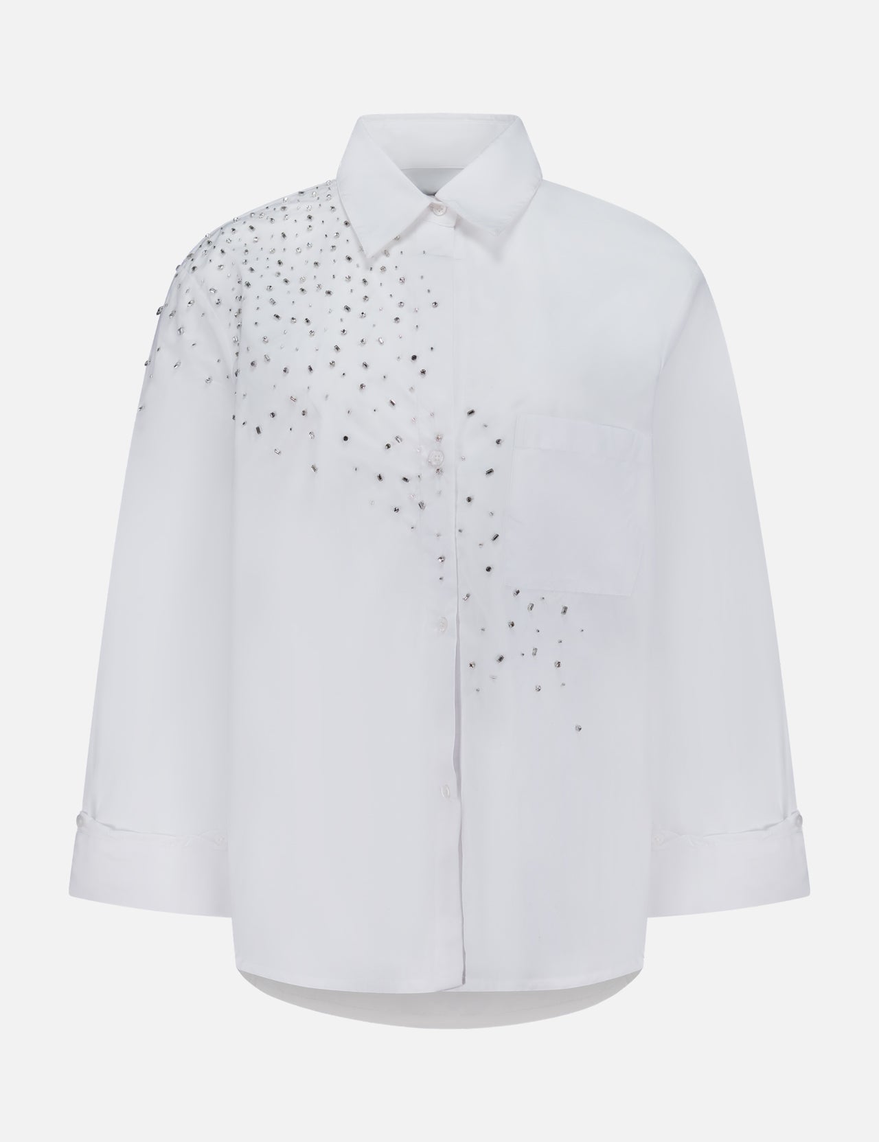The TWP Next Morning Crystal Shirt is a white oversized Italian cotton shirt with long sleeves and a chest pocket, adorned with a cluster of small silver studs that form embellished crystal detailing on the left shoulder and upper chest—offering both comfort and a modern, elevated edge.