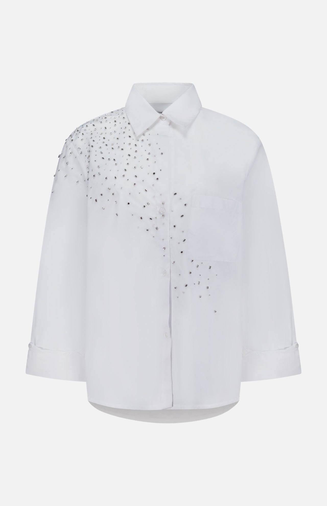 The TWP Next Morning Crystal Shirt is a white oversized Italian cotton shirt with long sleeves and a chest pocket, adorned with a cluster of small silver studs that form embellished crystal detailing on the left shoulder and upper chest—offering both comfort and a modern, elevated edge.