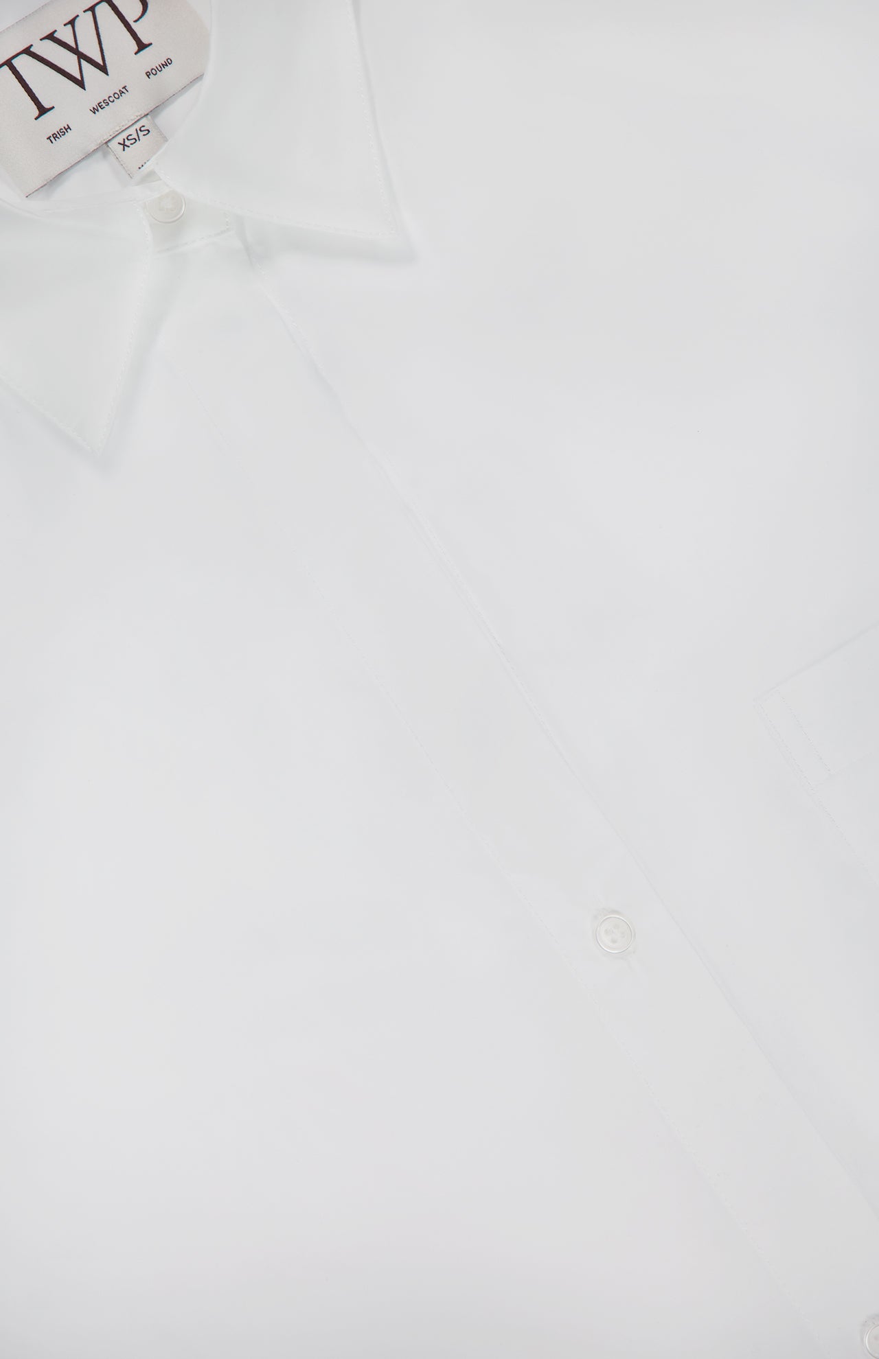 A close-up of the TWP Next Morning Oversized Shirt, crafted from Italian cotton with a pointed collar and visible buttons, featuring part of the label—an office chic staple.