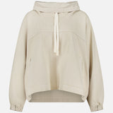 The Pull Me Over Jacket by TWP is a beige, long-sleeve hooded jacket featuring a front tie, two side pockets, and elastic cuffs—perfect as a versatile layering piece for women’s workwear—shown against a plain white background.