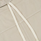 Close-up of the Pull Me Over Jacket by TWP in beige, featuring a V-shaped collar and two white, plastic-tipped drawstrings. The textured fabric and functional details elevate this women’s workwear staple with modern style.