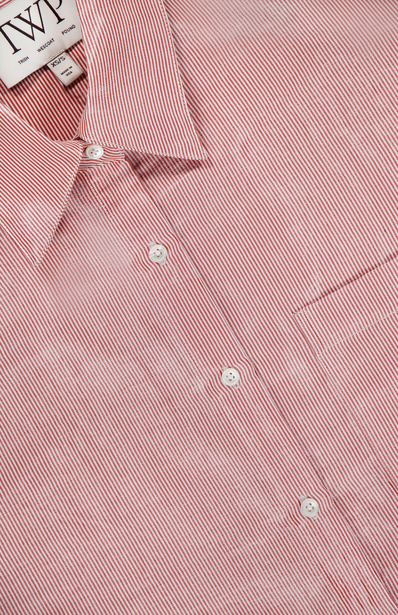 A close-up of the TWP Something Borrowed Striped Shirt, featuring red and white stripes, a collar, white buttons, and an inner label—an ideal women's workwear choice.