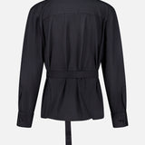 The Last Chapter Shirt by TWP is showcased from the back in black, featuring a long-sleeve belted silhouette with a collar, buttoned cuffs, and a straight hem. Expertly crafted from Italian wool twill, the fabric reveals a subtle texture that fuses classic women’s workwear with sophisticated tailoring. The shirt is presented against a plain white background.