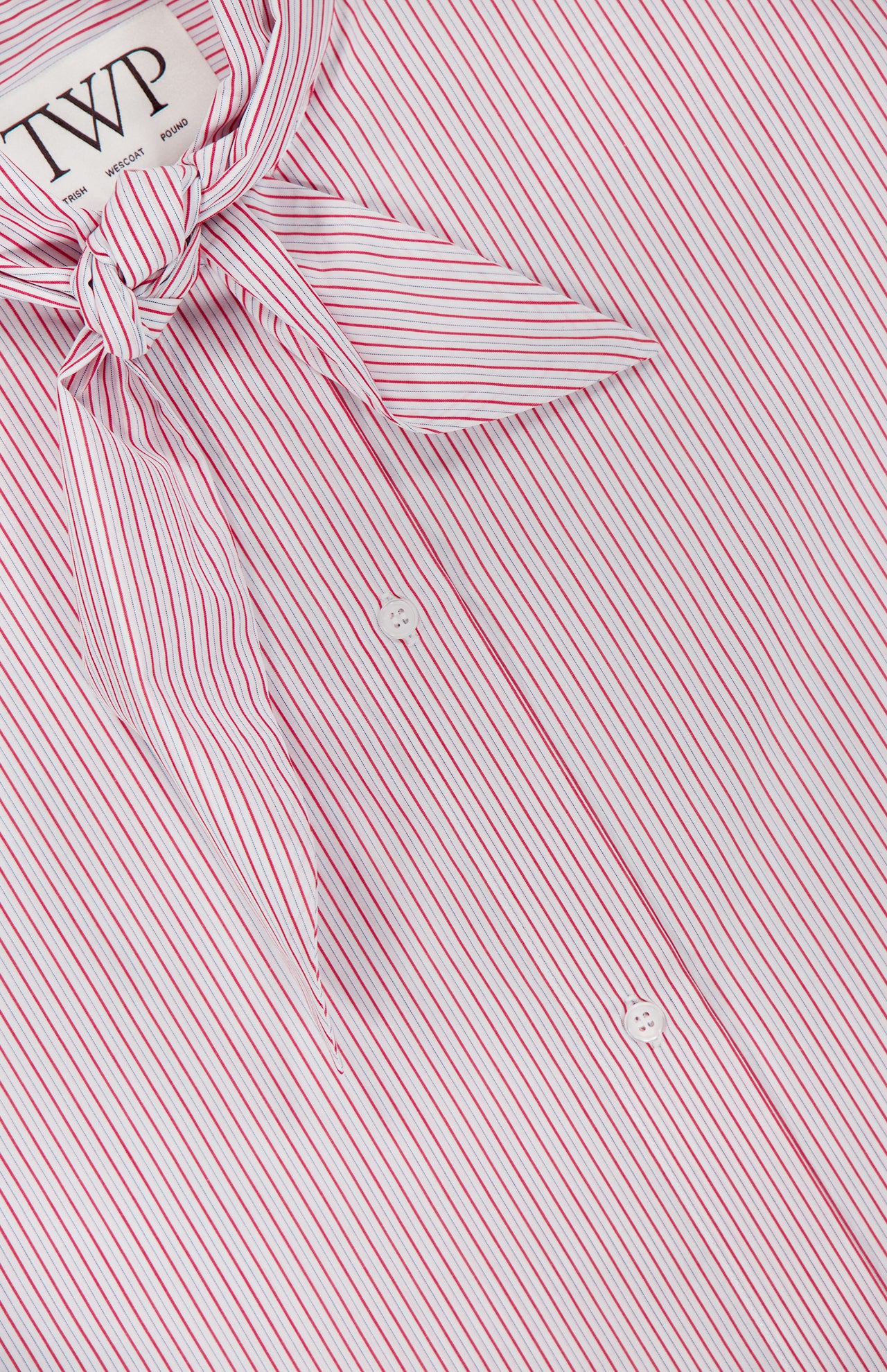 Close-up of the TWP Tie One On Striped Shirt, featuring pink and white vertical stripes, a matching tie at the collar, and two visible white buttons—an ideal workwear piece for women. The shirt label shows the TWP brand.