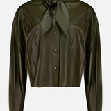 TWP’s Tied Up In You Shirt, a dark green button-up blouse with long sleeves, features an oversized neck tie and a shiny finish—an elevated take on classic women’s workwear, shown against a plain white background.